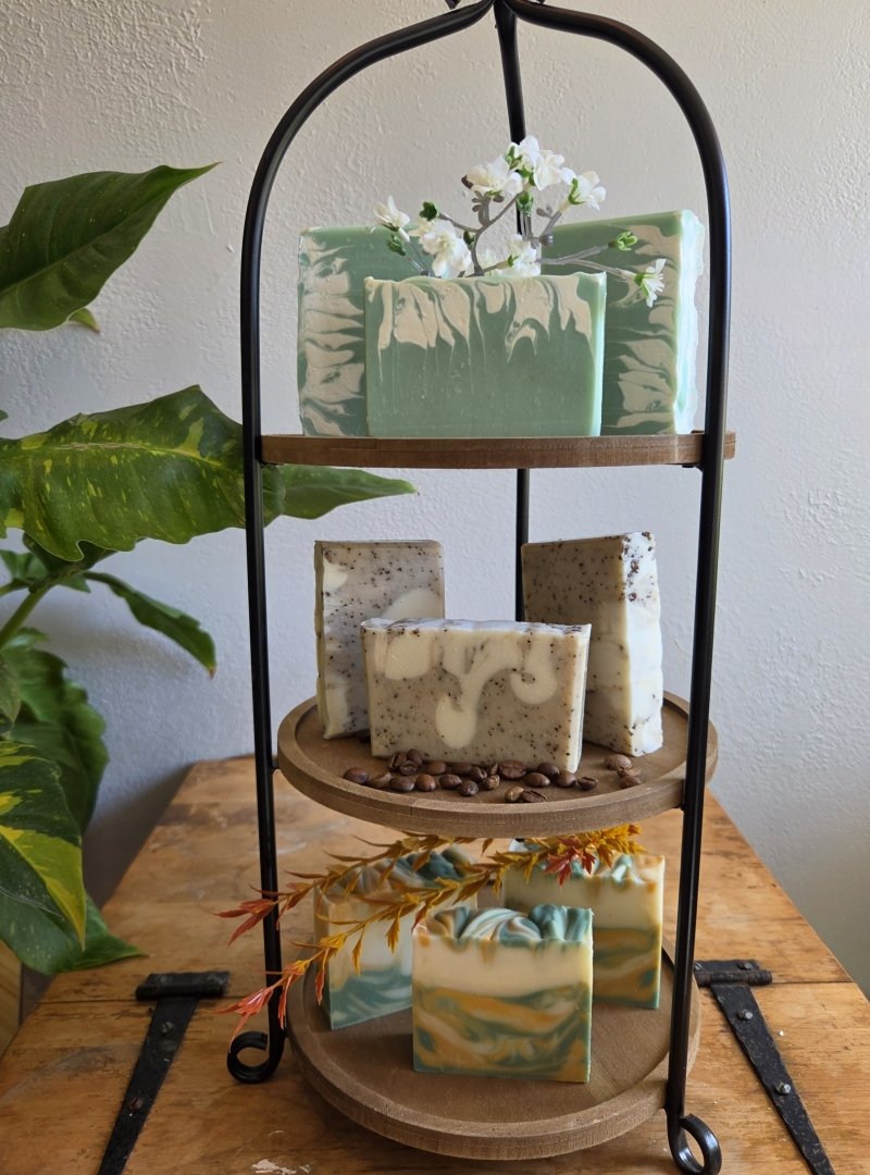 Bars of our soap displayed on a three-tier stand: green-swirled bars on top, coffee bars in the middle, and green and gold bars at the bottom.